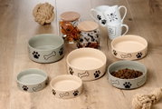 Verschiedene Hundenäpfe in Beige und Grau mit Pfoten- und Knochenmotiven, aus der Vogelperspektive auf einem Holzboden arrangiert.