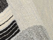 Nahaufnahme eines strukturierten Teppichs mit abstraktem Muster in Schwarz, Grau und Cremefarben, perspektivisch von oben fotografiert.