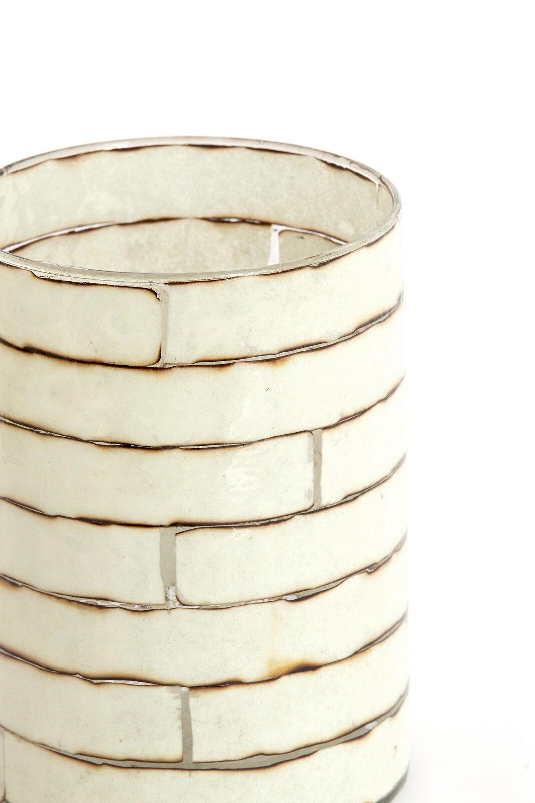 Nahaufnahme eines dekorativen Teelichthalters mit einem gestreiften, cremefarbenen Design und metallischen Akzenten, seitliche Perspektive.