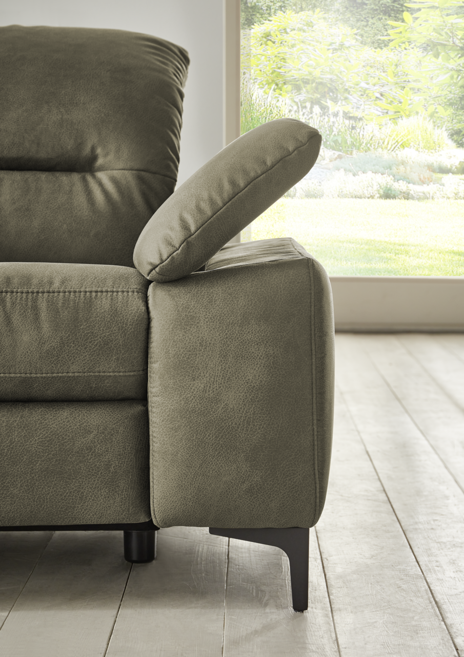 Nahaufnahme eines grünen Longchairs mit verstellbarer Armlehne, seitliche Perspektive, im Hintergrund ein Fenster mit Blick auf einen Garten.