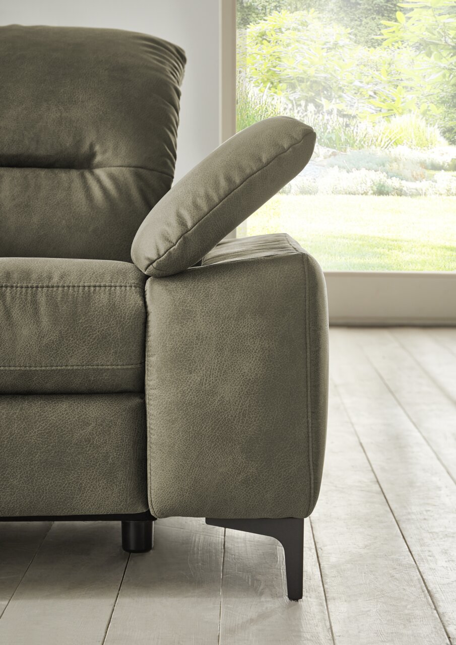 Nahaufnahme eines grünen Longchairs mit verstellbarer Armlehne, seitliche Perspektive, im Hintergrund ein Fenster mit Blick auf einen Garten.