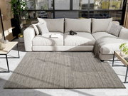 Grauer Wollteppich in einem modernen Wohnzimmer, fotografiert aus der Vogelperspektive, mit einem beigen Sofa und einem Couchtisch im Hintergrund.