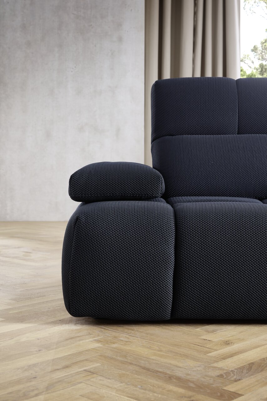 Nahaufnahme einer modernen, dunkelblauen Eckgarnitur mit strukturiertem Stoffbezug, seitliche Perspektive.