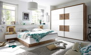 Moderne Schlafzimmermöbel mit einem weißen Schwebetürenschrank und einem Bett mit Holz- und Weißakzenten, seitliche Perspektive.