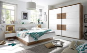 Moderne Schlafzimmermöbel mit einem weißen Schwebetürenschrank und einem Bett mit Holz- und Weißakzenten, seitliche Perspektive.