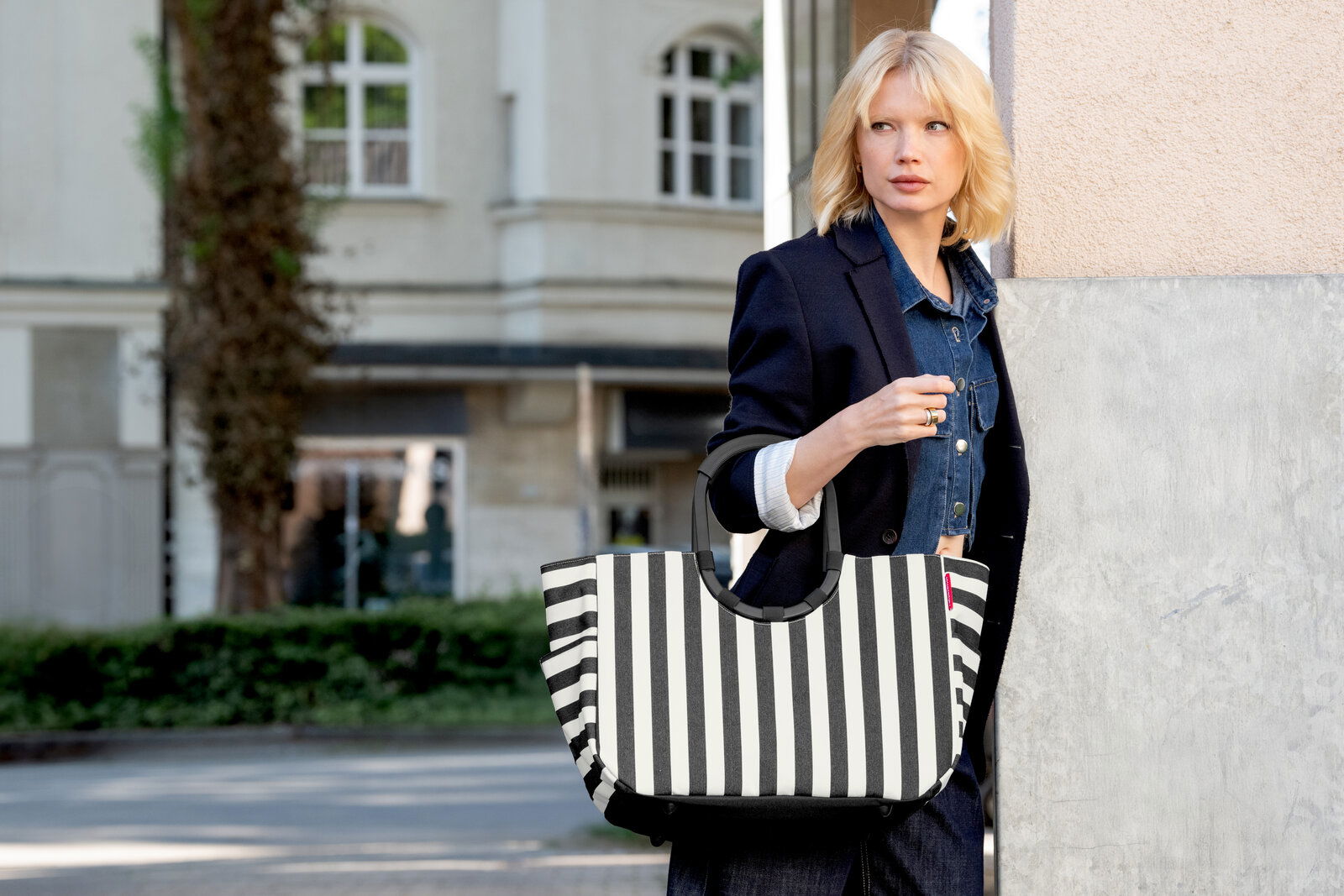 Schwarz-weiß gestreifte Handtasche mit kurzen schwarzen Henkeln, getragen von einer Frau im urbanen Außenbereich; Perspektive: frontale Ansicht auf die Tasche in leichter Seitenansicht.