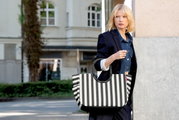 Schwarz-weiß gestreifte Handtasche mit kurzen schwarzen Henkeln, getragen von einer Frau im urbanen Außenbereich; Perspektive: frontale Ansicht auf die Tasche in leichter Seitenansicht.