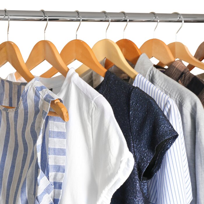 Kleding aan houten kleerhangers op een metalen kledingstang, met shirts en jurken in verschillende kleuren en patronen, frontale close-up perspectief