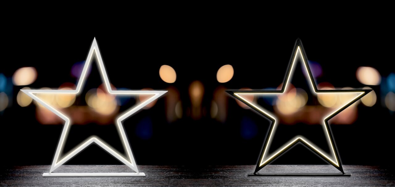 Zwei leuchtende LED-Sterne auf einem Tisch vor einem unscharfen, dunklen Hintergrund, frontal betrachtet.