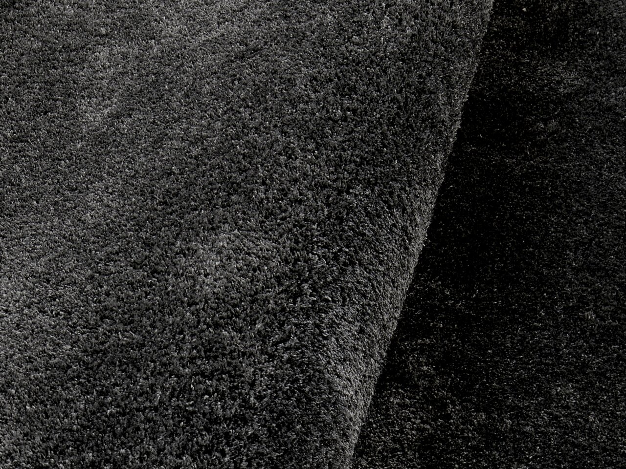 Nahaufnahme eines dunkelgrauen Hochflor-Teppichs in seitlicher Perspektive.