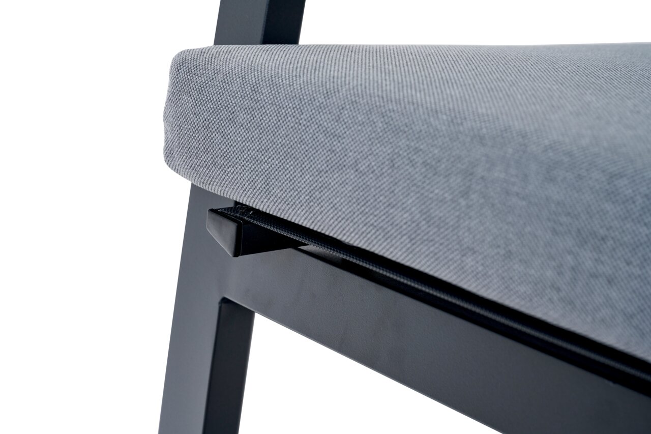 Close-up van een Comfort Plus stapelstoel met grijze bekleding en een zwart metalen frame, gezien vanaf de zijkant.