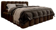 Gestoffeerd bedframe van bruine stof met doorgestikt hoofdeinde, gezien vanaf de zijkant, versierd met een geruite sprei en kussens.