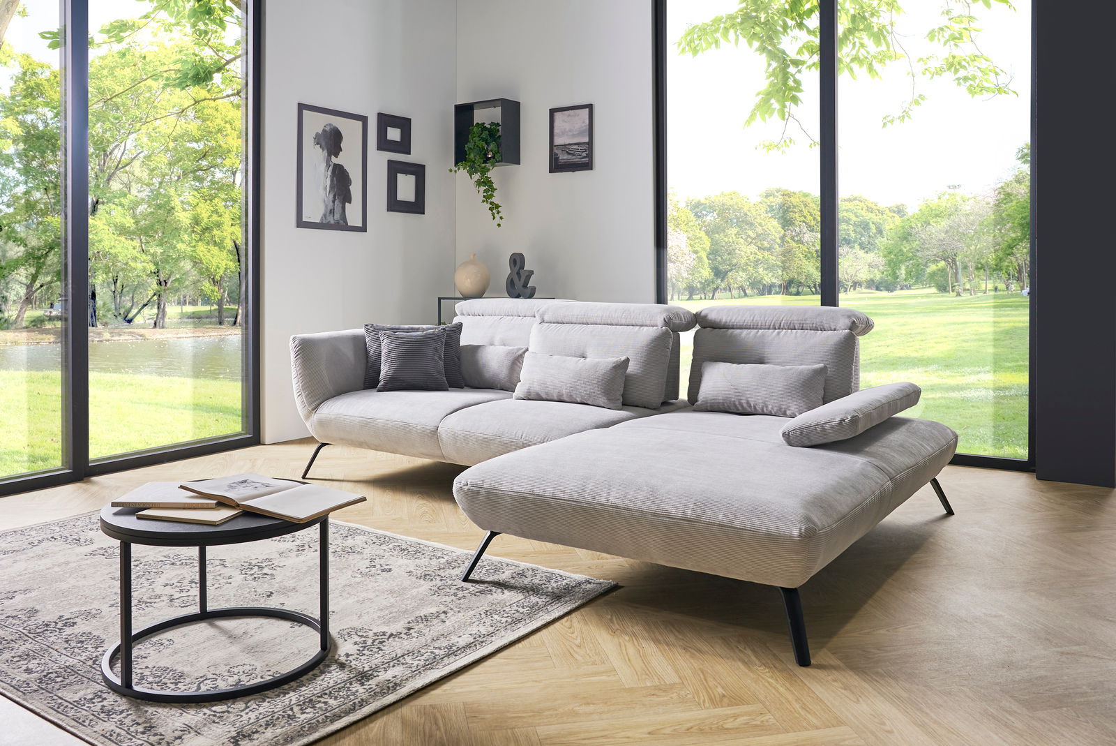 Moderne Rundecke in einem hellen Wohnzimmer mit großen Fenstern, die einen Blick ins Grüne bieten. Perspektive von vorne links.