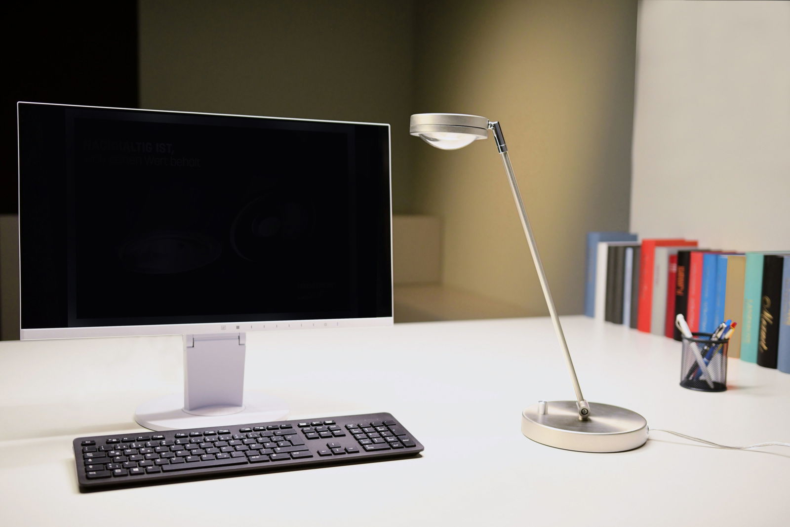 Megatron LED-Tischleuchte OTTICA Moderne LED Tischleuchte aus Metall in seitlicher Perspektive auf einem Schreibtisch neben einem Monitor und einer Tastatur.