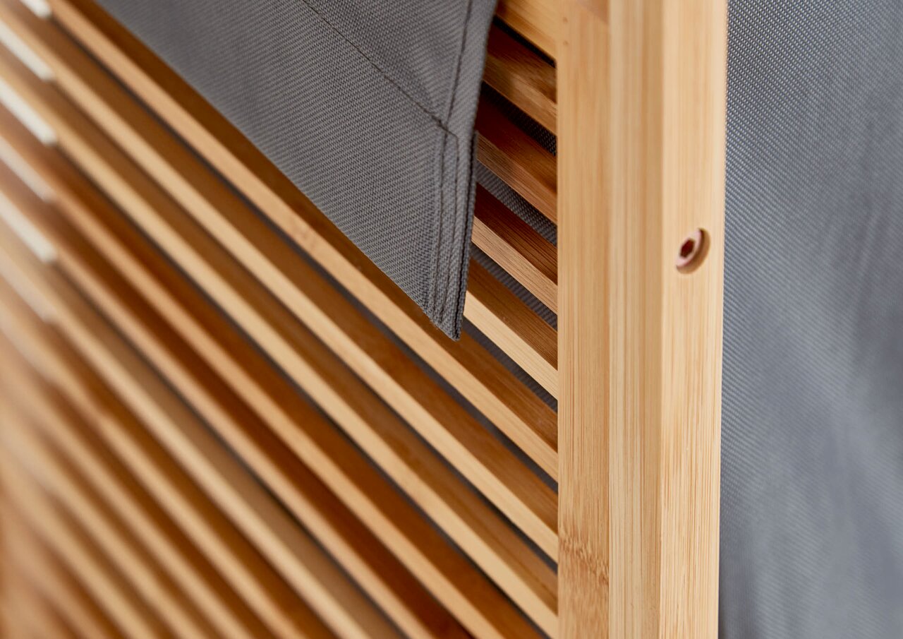Detailaufnahme aus schräger Seitenperspektive: Holzrahmen mit Lamellen und grauem Stoffbezug, Nahansicht der Kante und Befestigungsöffnung.