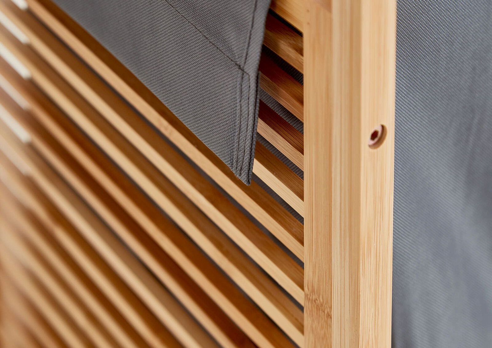 Detailaufnahme aus schräger Seitenperspektive: Holzrahmen mit Lamellen und grauem Stoffbezug, Nahansicht der Kante und Befestigungsöffnung.