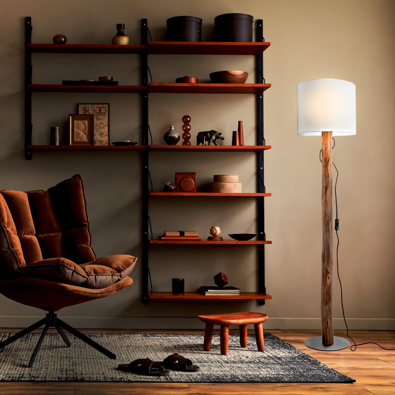 Stehleuchte mit natürlichem Holzstamm und weißem Lampenschirm, seitliche Perspektive im Wohnzimmer mit Regal und Sessel.