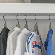 Kleding aan hangers in een open kledingkast: witte overhemden en een wit sportshirt met blauw-rode strepen naast een blauwe trui, frontaal aanzicht op ooghoogte.
