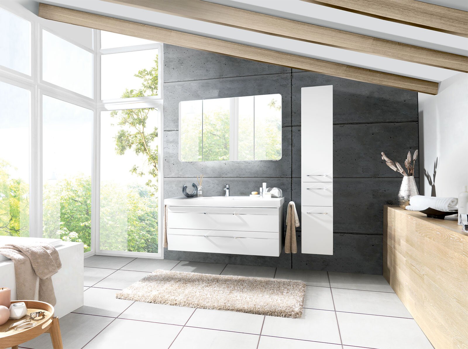 Modernes Badezimmer mit weißem Waschtisch mit zwei Schubladen, passendem Spiegelschrank und hohem Hochschrank vor grauer Betonwand, fotografiert in frontaler Perspektive mit leichter Weitwinkelansicht.
