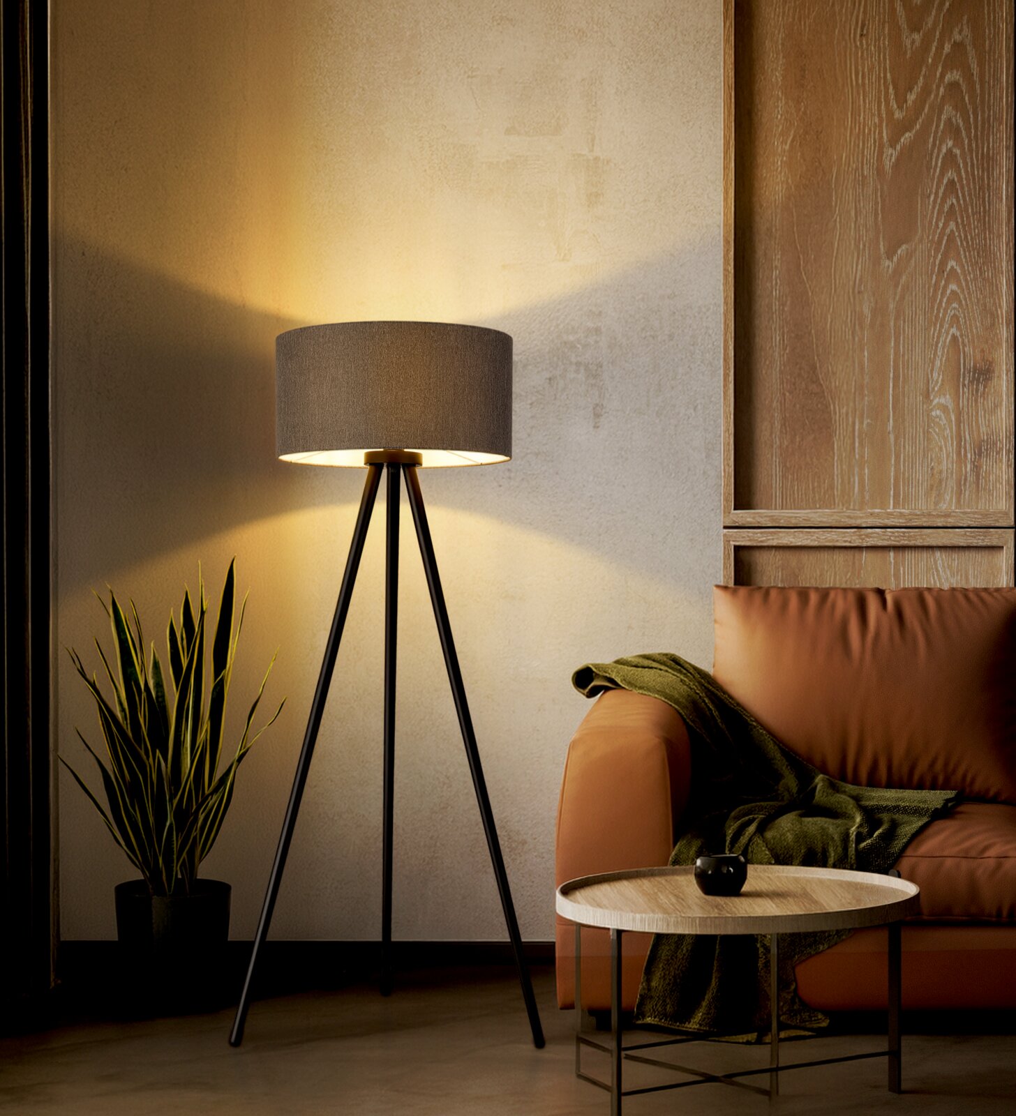 Moderne Tripod-Stehlampe mit schwarzem Dreibein-Gestell und grauem Stoffschirm, eingeschaltet neben einem braunen Sessel im Wohnzimmer, Frontansicht auf Augenhöhe