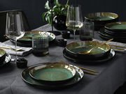 Elegantes 18-teiliges Tellerset in Grün auf einem gedeckten Tisch, seitliche Perspektive.