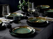 Elegantes 18-teiliges Tellerset in Grün auf einem gedeckten Tisch, seitliche Perspektive.