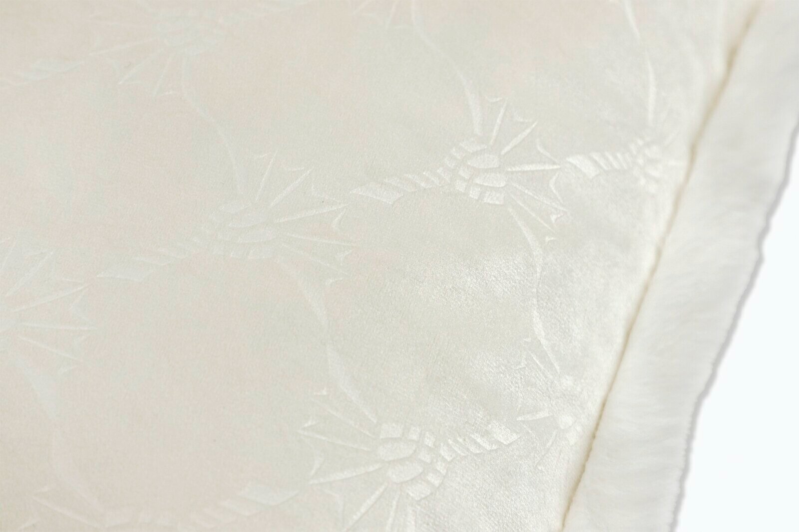 Nahaufnahme eines weißen, strukturierten Stoffes mit floralen Mustern und weichem Rand.