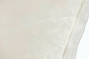 Nahaufnahme eines weißen, strukturierten Stoffes mit floralen Mustern und weichem Rand.