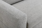 Detailansicht aus schräger Perspektive auf die breite Armlehne und Sitzfläche eines hellgrauen Sofas mit fein strukturierter Stoffpolsterung