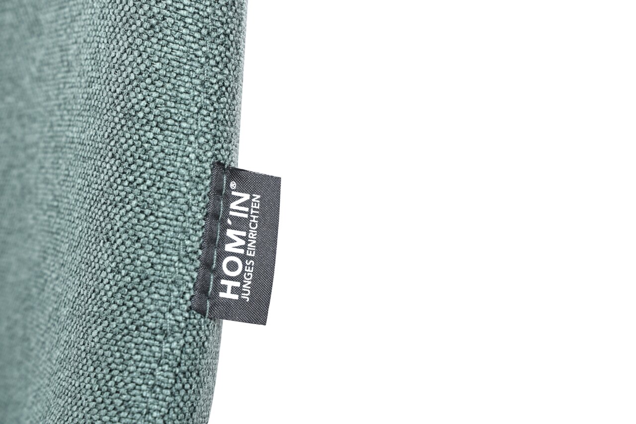 Nahaufnahme eines grünen Stoffes mit einem Etikett der Marke HOM'IN, seitliche Perspektive.