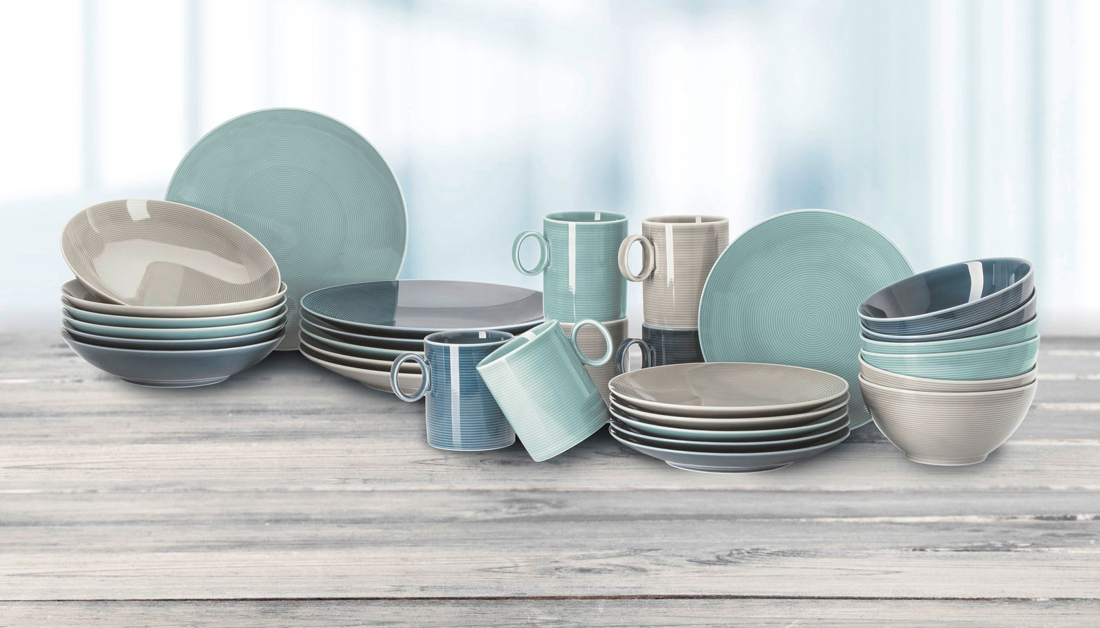 Thomas Kaffeeservice 18-tlg. LOFT NORDIC COLOURS Vielseitiges Tafelservice Loft in sanften Pastelltönen, bestehend aus Tellern, Schalen und Tassen, auf einer Holzoberfläche präsentiert, seitliche Perspektive.