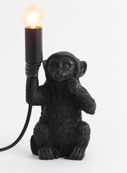 Schwarze Tischleuchte in Form eines Affen, der eine Glühbirne in der Hand hält, frontal betrachtet.