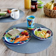 Frühstücksset für Kinder mit Teller, Schale und Becher, verziert mit bunten Pfotenabdrücken und einem Hundemotiv, auf einem Tisch von oben fotografiert.