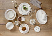 Vogelperspektive auf ein elegantes Kaffeeservice Isabella mit verschiedenen Tellern, Tassen und Besteck auf einem Holztisch.