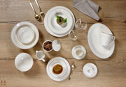 Vogelperspectief op een elegant Isabella-servies met diverse borden, kopjes en bestek op een houten tafel.