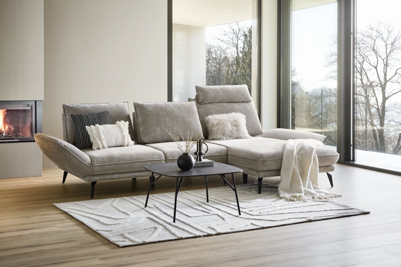 Moderne longchair-bank in een elegante woonkamer met open haard en grote ramen, gezien vanaf de zijkant.
