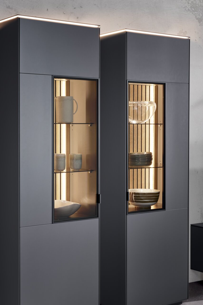 Moderne Vitrine mit Glasfronten, beleuchtetem Innenraum und stilvoller Präsentation von Geschirr, seitliche Perspektive