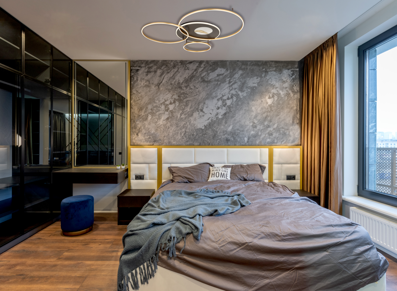 Moderne Deckenleuchte INVERTINA mit kreisförmigem Design, von unten betrachtet in einem stilvollen Schlafzimmer mit grauer Akzentwand und großen Fenstern.