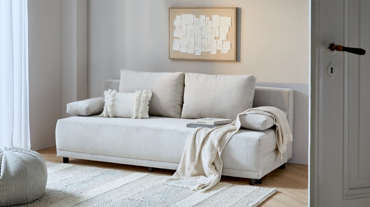 Beiges Funktionssofa in einem modernen Wohnzimmer, frontal fotografiert, mit Kissen und Decke dekoriert.