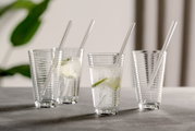 Vier durchsichtige Becher mit Spiraldesign und Trinkhalm, gefüllt mit sprudelndem Wasser und Limettenscheiben, auf einer grauen Oberfläche. Seitliche Perspektive.
