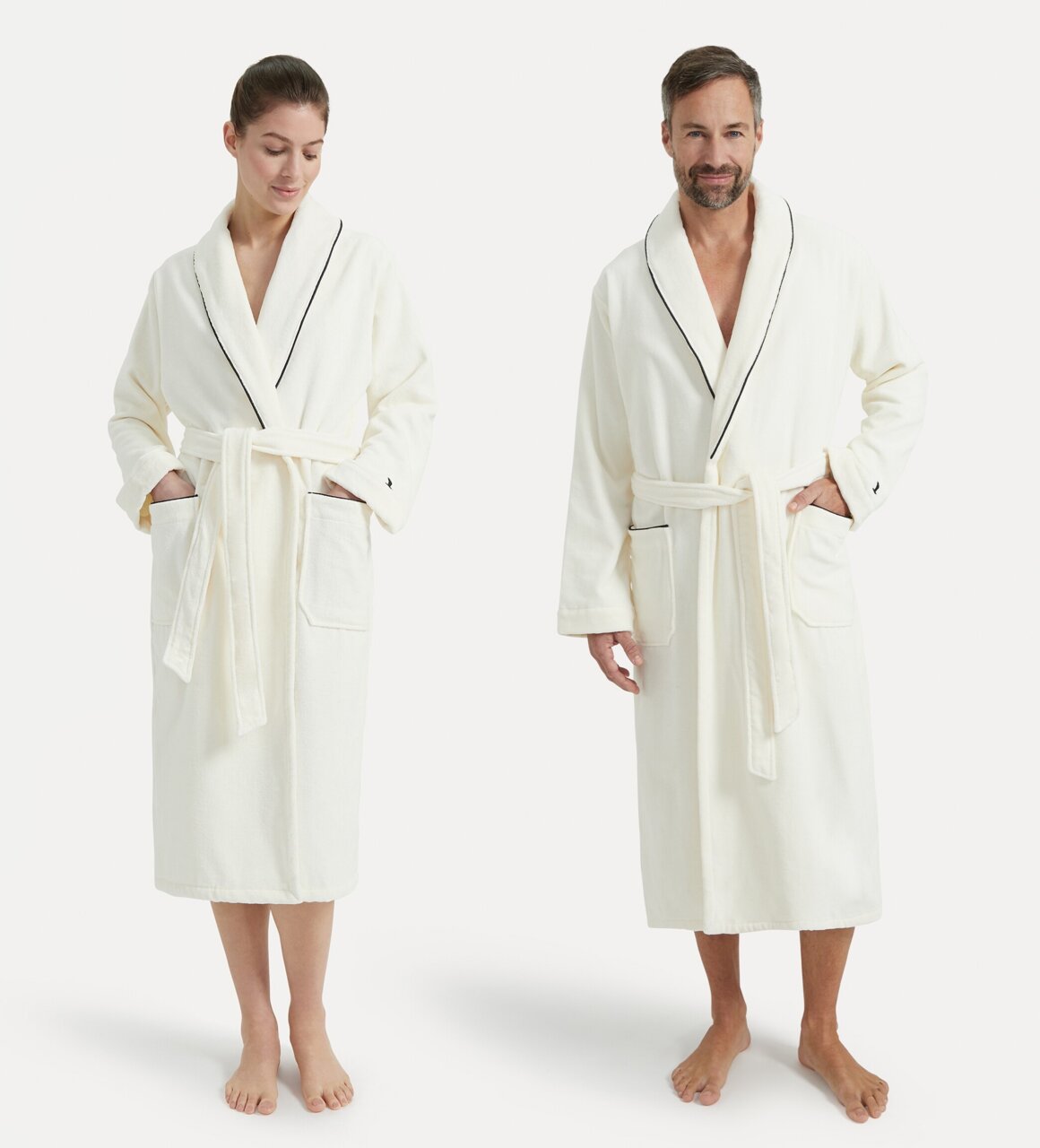 Zwei Personen tragen einen weißen Bademantel mit Schalkragen und schwarzer Paspelierung, frontal fotografiert.