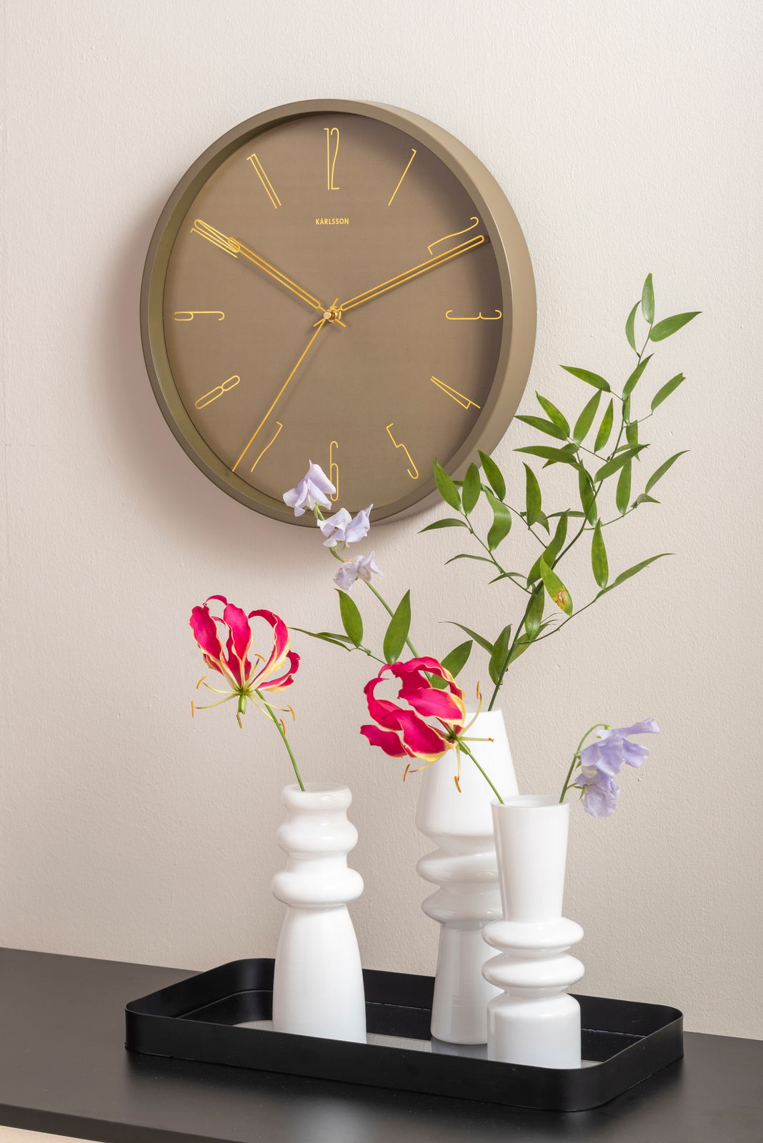 Wanduhr Belle Numbers aus Metall in Seitenansicht, mit goldenen Zeigern und Ziffern auf braunem Zifferblatt, dekoriert mit Blumen in weißen Vasen.