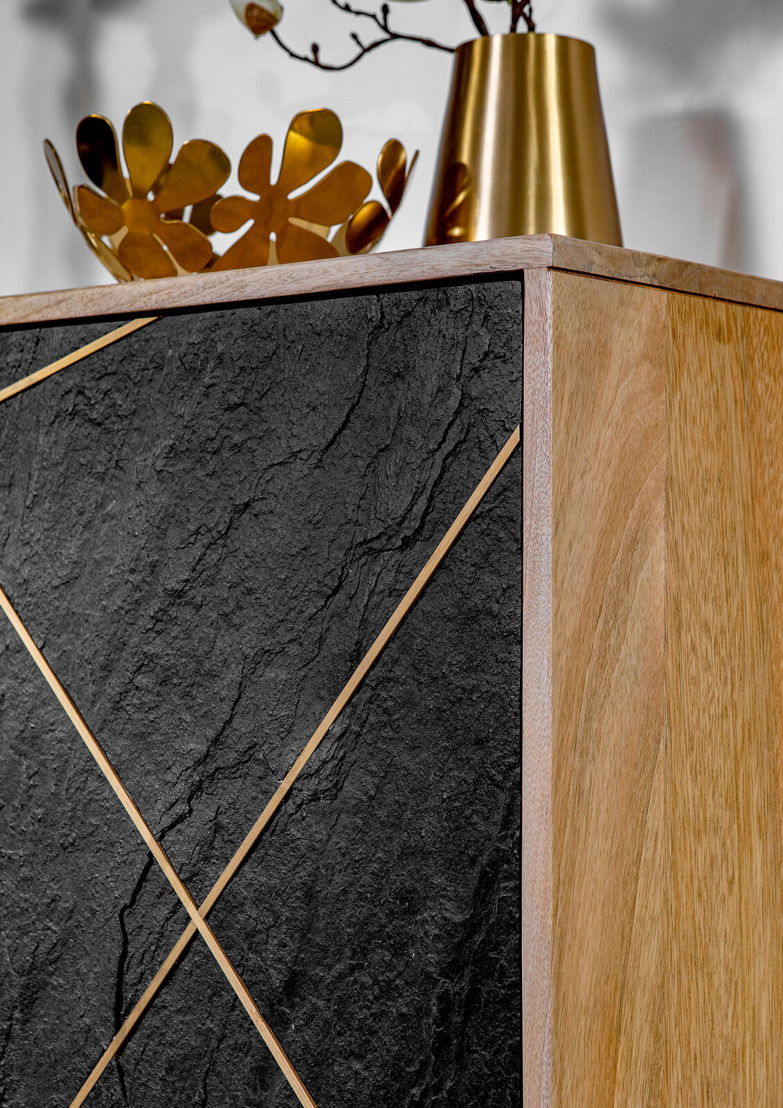 Detailansicht einer Kommode mit schwarzer Steinoptik und goldenen Akzenten, kombiniert mit einer Holzseite. Obenauf stehen goldene Dekorationsgegenstände.