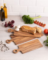 Holzgriffbrett 20x50x1,5 cm in einer Küchenumgebung, umgeben von frischen Zutaten wie Brot, Knoblauch, Zwiebeln, Tomaten und Kräutern. Draufsicht.