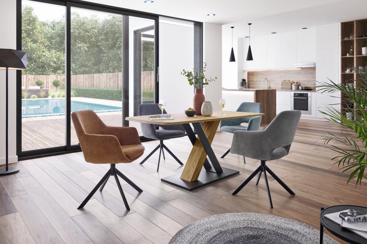 Moderner Esstisch mit X-förmigem Gestell aus Holz und Metall, umgeben von gepolsterten Stühlen in einem hellen, offenen Wohnbereich mit Blick auf den Garten. Perspektive: seitlich.