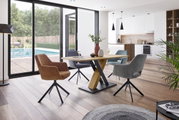 Moderner Esstisch mit X-förmigem Gestell aus Holz und Metall, umgeben von gepolsterten Stühlen in einem hellen, offenen Wohnbereich mit Blick auf den Garten. Perspektive: seitlich.