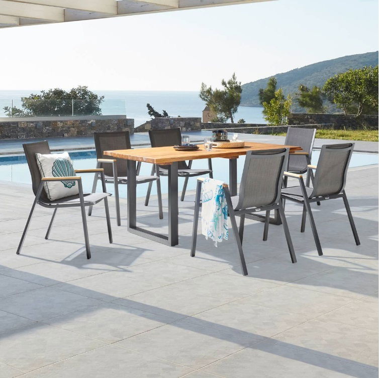 Moderner Stapelsessel aus Metall und Textil, aufgestellt auf einer Terrasse mit Blick auf das Meer, umgeben von einem Tisch und weiteren Stühlen.