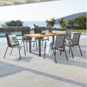 Moderner Stapelsessel aus Metall und Textil, aufgestellt auf einer Terrasse mit Blick auf das Meer, umgeben von einem Tisch und weiteren Stühlen.