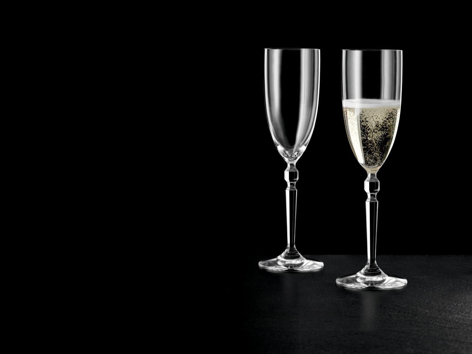 Zwei elegante Champagnerflöten aus klarem Glas auf schwarzem Hintergrund, eine leer und eine mit Sekt gefüllt, frontale Produktansicht
