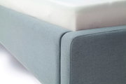 Nahaufnahme eines blauen Polsterbetts mit sichtbarer Matratze, seitliche Perspektive.